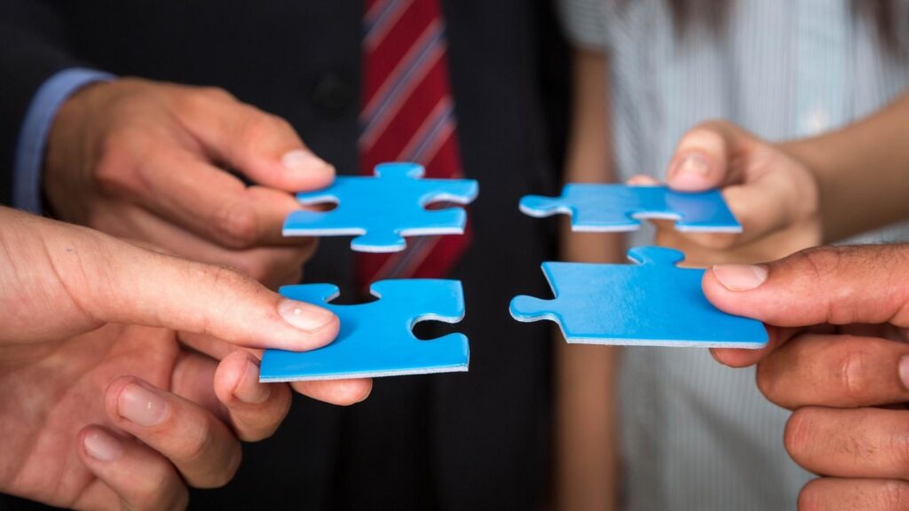 Business people holding jigsaw pieces to symbolise a merger.